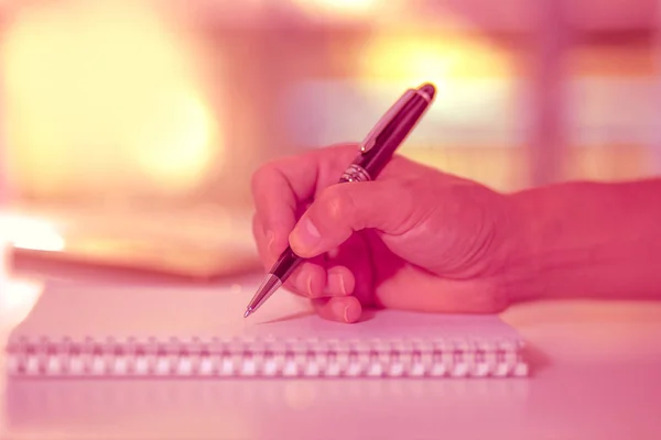Man hand holding a pen writing on the notebook.