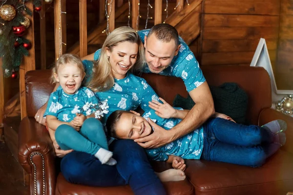 Család - anya, apa, fia és lánya - játszik és mosolyog a kanapén a fa barna nappaliban — Stock Fotó