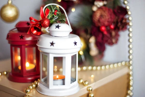 Винтажные рождественские фонари красного и белого цвета с горящими свечами. Уютные рождественские украшения с золотыми бусами и шариками. Рождественская елка на фоне . — стоковое фото