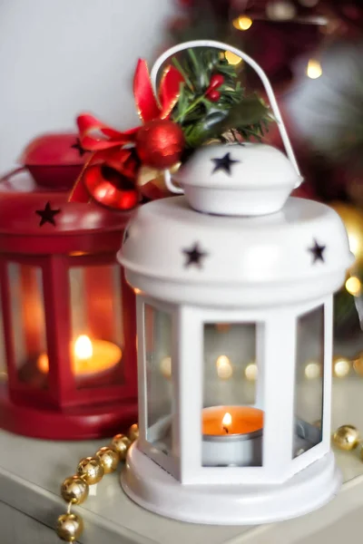Винтажные рождественские фонари красного и белого цвета с горящими свечами. Уютные рождественские украшения с золотыми бусами, шарами. Рождественская елка на фоне — стоковое фото
