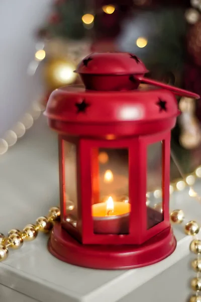 Vintage Christmas Lantern Red with burning Candles. Cozy christmas decorations with golden beads, balls. Christmas tree on background