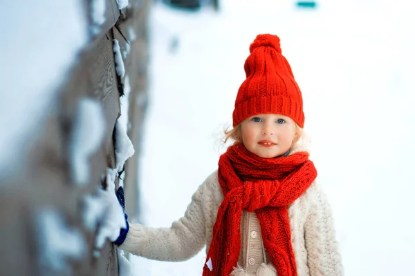 Ragazzina divertente con cappello e sciarpa in maglia rossa e pullover bianco che gioca all'aperto in inverno. I bambini giocano all'aperto in inverno. I bambini si divertono nel periodo natalizio. Divertimento invernale — Foto Stock