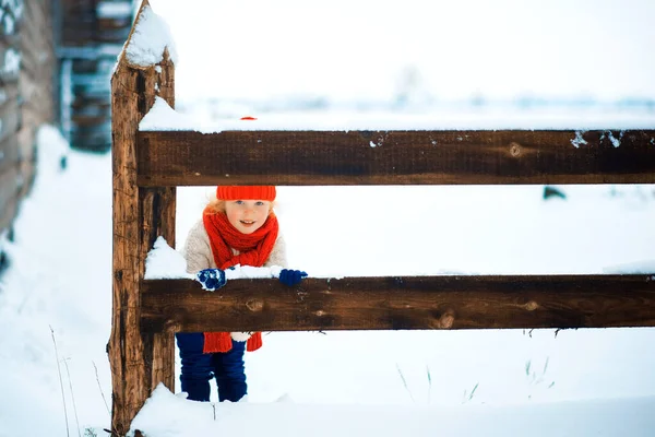 Petite fille drôle dans un chapeau tricoté rouge et écharpe et pull blanc jouant à l'extérieur en hiver. Les enfants jouent dehors en hiver. Les enfants s'amusent à Noël. Amusement d'hiver — Photo