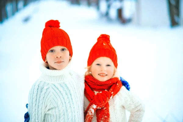 Drôle de petite fille et garçon dans un chapeau tricoté rouge et écharpe et pull blanc jouant à l'extérieur en hiver. Les enfants jouent dehors en hiver. Les enfants s'amusent à Noël. Frère et sœur . — Photo