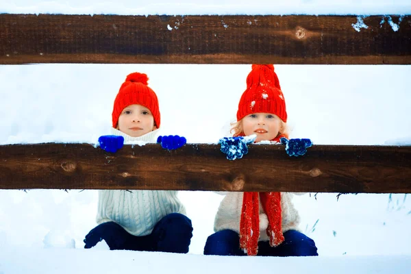 Drôle de petite fille et garçon dans un chapeau tricoté rouge et écharpe et pull blanc jouant à l'extérieur en hiver. Les enfants jouent dehors en hiver. Les enfants s'amusent à Noël. Frère et sœur . — Photo