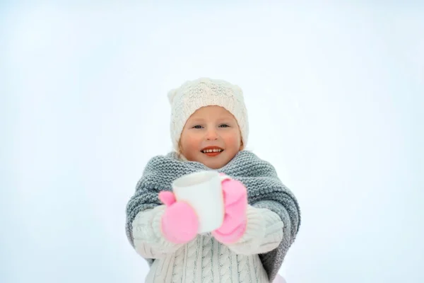 Molto dolce bella bambina sorridente in gonna rosa e guanti, pullover bianco, sciarpa grigia e cappello bianco con coppa bianca in mano. Spazio per testo — Foto Stock