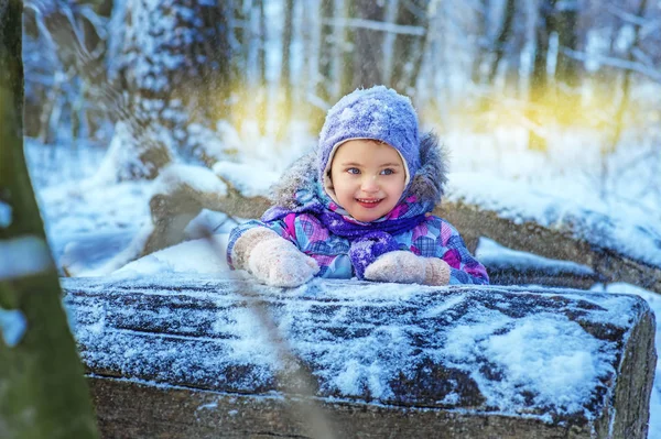 小个子4岁的日本女孩在雪地的冬季森林里户外玩耍。 穿着五颜六色衣服的孩子笑着把目光移开. 木箱在女孩面前。 日落时分 — 图库照片