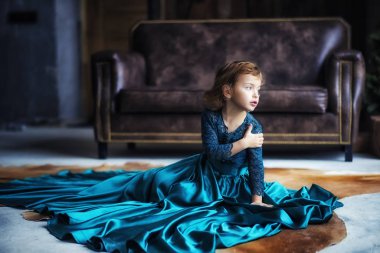 5 yaşında harika bir nane şekeri elbisesi giymiş genç bir kız kanepenin yanında oturuyor ve başını çeviriyor. Çocuk tek eliyle kendini kucaklıyor.