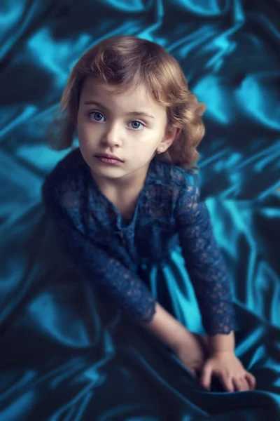 Νέοι 5 ετών κορίτσι σε vintage υπέροχο φόρεμα μέντας κάθεται στο πάτωμα και κοιτάζει προς τα πάνω στην κάμερα. Το παιδί σκέφτεται και φαίνεται σοβαρό. Εσωτερικά — Φωτογραφία Αρχείου
