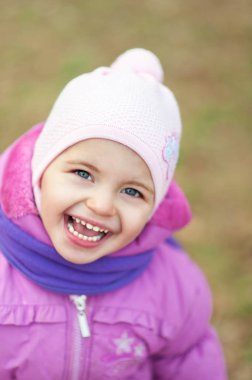 2 yaşında, pembe ceketli, pembe şapkalı ve açık havada duygusal ifadeli menekşe eşarplı bir çocuk. Sonbahar sonbahar kız portresi. Sonbahar ve ilkbaharda sıcak giysiler. Doğal ışık