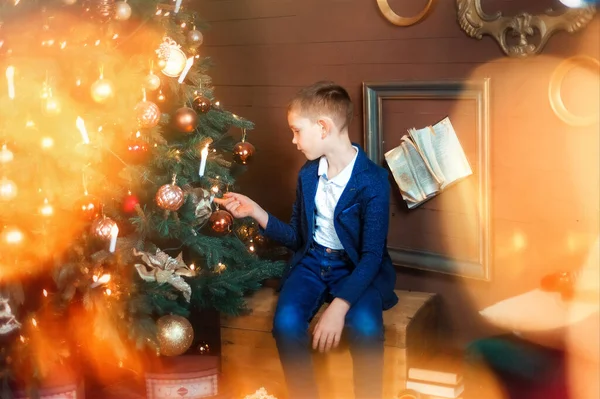 Garçon de 6 ans s'asseoir et regarder beau sapin de Noël. Des lumières de Noël. Veilles de Noël et cadeaux. Enfant attendre des cadeaux dans la nouvelle année. Sérieux enfant triste — Photo