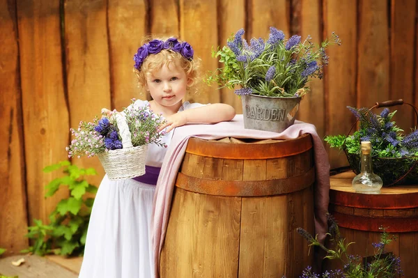 Niña en ropa blanca y corona violeta en decoraciones de estilo rústico. Ecología. Estilo de vida orgánico y ecológico en la infancia. Fondo de madera y flores alrededor. Niño en vestido antiguo — Foto de Stock