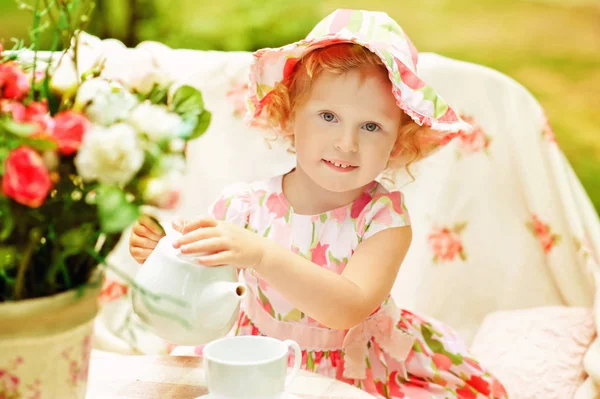 Niña de 3 años en vestido rosa y sombrero rosa juegan afuera. La joven vierte té de tetera en taza. Verano. Piquenique al aire libre. Juego de niños en la vida adulta. Hora del té. Estilo de vida cerca de la naturaleza — Foto de Stock