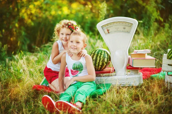 Zwei Geschwister spielen in Wassermelonenverkäufern mit großen altmodischen weißen Schuppen. emotionale Kinder Mädchen umarmen Jungen mit großen Wassermelonen im Park. gesunde Biolebensmittel für Kinder. — Stockfoto