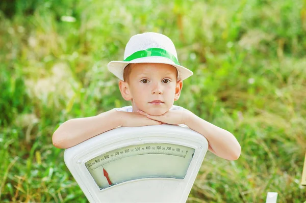Yazlık şapkalı 5 yaşında bir çocuk elleri beyaz pulların üzerinde yerde oturuyor. Yaz zamanı. Çocuklar yazın dışarıda oynarlar. Ağırlıkları dışarıda olan ciddi bir çocuk. Doğaya yakın çocukluk — Stok fotoğraf