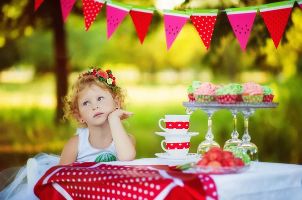 Pequeña niña de 3 años de edad sueñan con comer magdalena, pero pensar en una dieta saludable. Niña rechazando comida chatarra. Niña pequeña espera a los invitados en su fiesta de cumpleaños. Deliciosos pastelitos coloridos — Foto de Stock