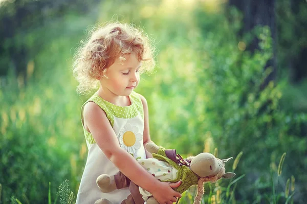 Πορτρέτο του 3 ετών μικρή σγουρή ξανθιά όμορφη σοβαρή κοπέλα με παιχνίδι στα χέρια της. Παιδί στο φως του ηλιοβασιλέματος μείνετε στον κήπο. Χώρος για κείμενο. Μικρό παιχνιδιάρικο κορίτσι στο πάρκο. παιδί κοντά στη φύση. — Φωτογραφία Αρχείου