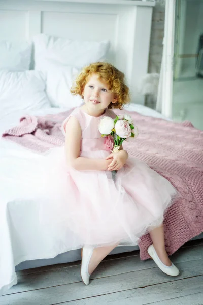 Retrato de niña rizada rubia sonriente de 5 años en vestido de princesa con ramo de flores rosadas en sus manos sentadas en mal estado. Niña en su cumpleaños esperando regalos. Primavera. Día de la mujer — Foto de Stock