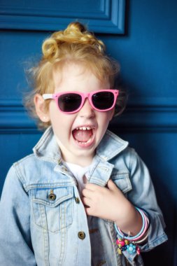 Kıvırcık saçlı, kot ceketli, pembe gözlüklü ve mavi stüdyoda bir sürü bileziği olan küçük bir kız. Çocukluğundaki hippi yaşam tarzı. Şık bir çocuk. Çocuklar için moda.