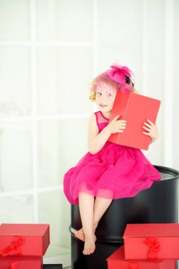 4 yaşında, güzel pembe elbiseli, peçeli pembe şapkalı, elinde hediyelerle elinde kırmızı bir hediye kutusuyla siyah fıçıda oturan küçük bir kız. Doğum günü kızı doğum günü partisinde arkadaşlarını bekliyor..
