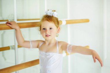 4 yaşındaki sarışın, kıvırcık balerin. Bale stüdyosunun yanında dans ediyor. Bale elbisesi içinde ve başka tarafa bakıyor. Sıkı dans etmek. Çocuklukta aktif yaşam tarzı.