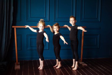 Üç küçük çocuğun portresi iki kız balerin ve dans stüdyosundaki bale barında çalışan siyah taytlı küçük erkek dansçı. Dans eden çocuklar. Çocuklukta aktif yaşam tarzı.