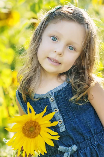 Zamknij portret 5-letniej dziewczyny z niebieskimi oczami w polu słoneczników z dużym słonecznikiem w rękach. Alergia latem. Alergiczne dzieci. Szczęśliwego dzieciństwa blisko natury. Styl życia — Zdjęcie stockowe