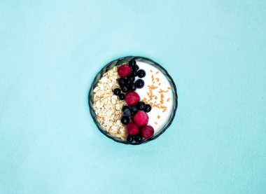 Sağlıklı organik vejetaryen kahvaltısı, bir kase müsli ve yoğurt, taze çilek, frenk üzümü ve mavi arka planda vişne. Bahar ve yazdan önce diyet