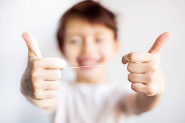 Diş ipinin çocuk ellerinde yakınlaştırılması. Beyaz tişörtlü mutlu çocuk odaktan çıkmış diş ipini iki eliyle tut. Diş ve sağlık sigortası. Çocukluktan kalma diş bakımı hayat boyu saklar..
