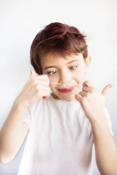Vertikální portrét překvapil dítě v bílém tričku, které úžasně vypadá na zubní nit pro zuby na bílém pozadí izolované. Zdravotní a zubní péče od dětství. Jak se používá zubní nit. — Stock fotografie