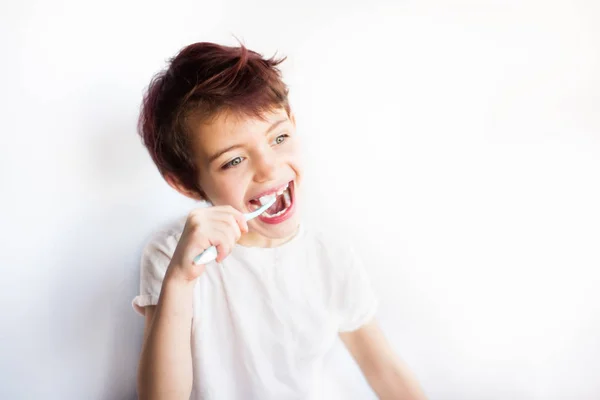 Gülümseyen çocuğun mavi ve beyaz diş fırçasıyla dişlerini fırçalarken ve başka tarafa bakarken yatay portresi. Çocukluktan kalma diş ve sağlık hizmetleri. Gülümseyen suratta sağlıklı dişler. Beyaz arka plan. Boşluğu kopyala — Stok fotoğraf