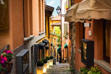 Bellagio kasabasında turuncu binalar ve fenerlerle dolu dar bir sokak ünlü İtalyan gölü Como, Lombardy, Kuzey İtalya 'da taş basamakları ve arka planda Alp dağlarıyla.