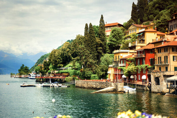Amazing view of Como Lake and Varenna, panorama of lake with small town and Alps mountains on background in cloudy day. Vacation on Como, Lombardy, Italy. Popular tourist destination. Italian city