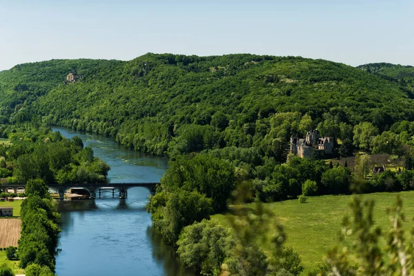 Uitzicht op de Dordogne rivier in de Dordogne vallei met Castelnaud-la-Chapelle kasteel aan de rechterkant van de foto en oude stenen brug in de zomerdag. Reisbestemming Aquitaine, Frankrijk — Stockfoto