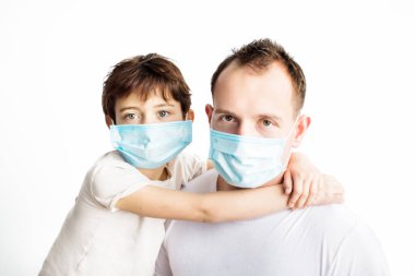 Child and dad in blue medical masks and white t-shirts hugging each other and looking in camera on white background. Coronavirus protection. Medical care. Illness covid-2019 prevention