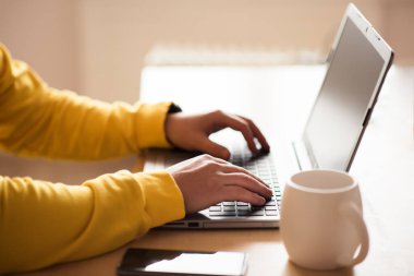 Adam evde dizüstü bilgisayarda yazı yazan sarı eşofman üstü, evde çalışan, internet konsepti olan bir adam. Karantina, izolasyon ve salgın sırasında evden çalışma Coronavirus covid-2019