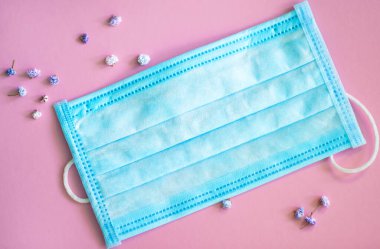 Tıbbi yüz maskesi. Etrafında küçük çiçekler olan pembe arka planda tıbbi koruyucu maske. Tek kullanımlık cerrahi maske. Sağlık ve tıbbi konsept. Coronavirus covid-2019 'dan koruma.