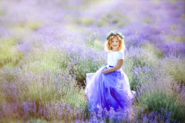Lavanta tarlasında lavanta rengi elbise ve çelenk giyen, güneşli yaz günlerinde eteğini mor çiçeklerle tutan mutlu, tatlı, sarışın kıvırcık kız. Tipik provenkal manzaradaki çocuk.