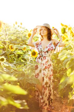 Hasır şapkalı kızıl saçlı güzel bir kadının dikey resmi. Arka plandaki ayçiçeği tarlasında. Yaz kırsal konsepti. Doğa tatiline yakın. Kadın ve ayçiçekleri. Yaz ışığı. Açık havada..