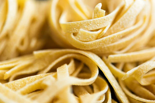 Geleneksel İtalyan çiğ makarnası Tagliatelle 'in Macro resmi, seçici odak görüntüsü. Vejetaryen yemeği. Beslenme konsepti. İtalyan mutfağı. Yemek hazırlama. Yemek makarna arka planı. Duvar kağıdı. Lezzetli.