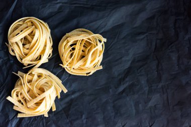 Üç parça geleneksel İtalyan çiğ makarnasının resmi siyah buruşmuş kağıt zemin üzerinde Tagliatelle makarnası, seçici odaklanma. Vejetaryen yemeği. Beslenme konsepti. İtalyan mutfağı. Hazırlık