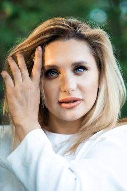 Güzel sarışın bir kadının dikey portresi. 30 yaşında. Makyajlı ve eli yüzüne yakın bir kadın. Kız bahar portresi. 30 yaşında cilt bakımı.