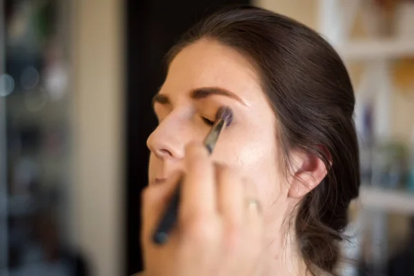 Backstage scene: Professional Make-up artist doing model makeup at work. Makeup Artist applies Eye Shadow. Beautiful Woman Face. Perfect Makeup. Make-up detail.