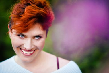 30 yaşında, kısa saçlı, açık havada gülümseyen beyaz bir kadının yakın plan portresi. Geniş gözenekli cilt makyajı. Cilt bakımı. Duygusal kızıl saçlı kız..