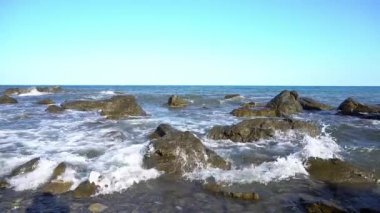 Denizin kayalık kıyılarında. Dalgalar gürültüyle kayalık bir kıyıya yuvarlanır. Deniz kenarında gün doğumu. Güzel deniz manzarası. Fırtınalı bir okyanusun kayalık kıyısı. Dalgalar kıyıya vuruyor.