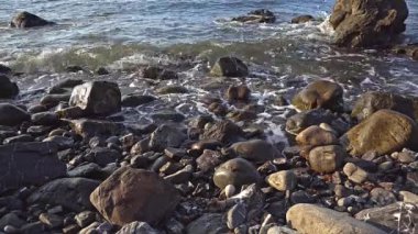 Denizin kayalık kıyılarında. Dalgalar gürültüyle kayalık bir kıyıya yuvarlanır. Deniz kenarında gün doğumu. Güzel deniz manzarası. Fırtınalı bir okyanusun kayalık kıyısı. Dalgalar kıyıya vuruyor.