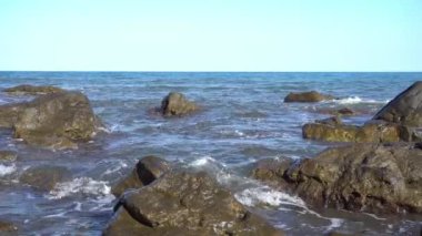 Denizin kayalık kıyılarında. Dalgalar gürültüyle kayalık bir kıyıya yuvarlanır. Deniz kenarında gün doğumu. Güzel deniz manzarası. Fırtınalı bir okyanusun kayalık kıyısı. Dalgalar kıyıya vuruyor.