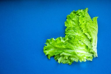 Yeşil salata mavi dackground üzerinde bir kalp şeklinde serilmiş.