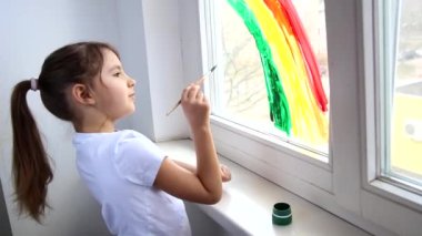 Covid-19 karantinası sırasında çocuk pencereye gökkuşağı çiziyor. Gökkuşağı flaş çetesini kovala ve ev konseptinde kal