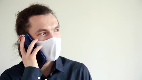 Um homem barbudo com uma máscara protectora está a falar ao telefone. Comunicação e trabalho remotamente durante a quarentena da pandemia COVID-19 . — Vídeo de Stock